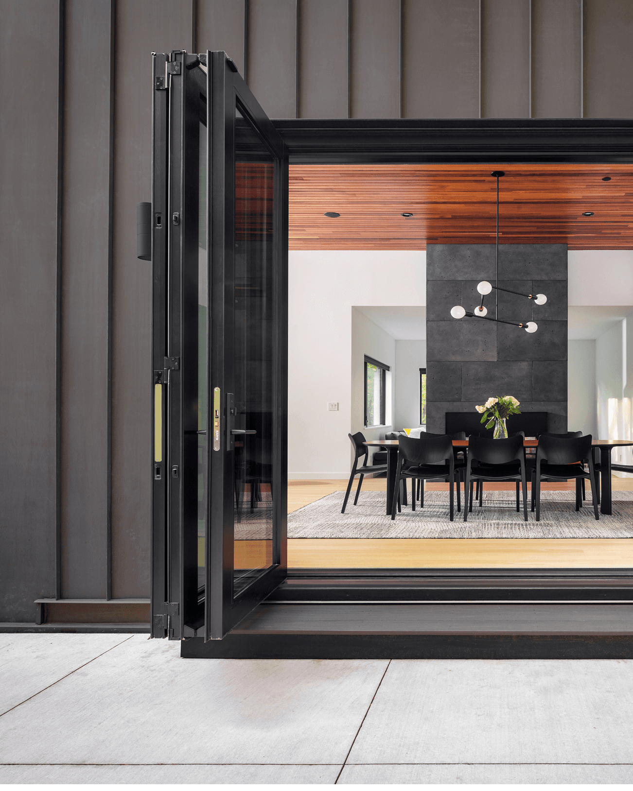 Home exterior looking into a dining room with an opened black Marvin Ultimate Bi-Fold Door.